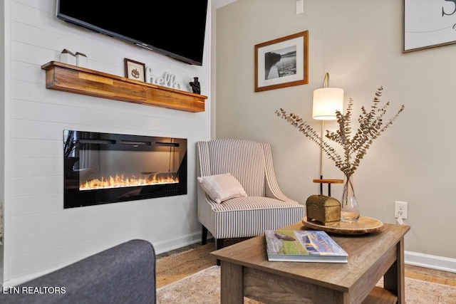 living area with light wood-type flooring, a glass covered fireplace, and baseboards