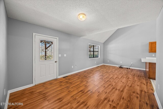 entryway with lofted ceiling, a textured ceiling, wood finished floors, visible vents, and baseboards