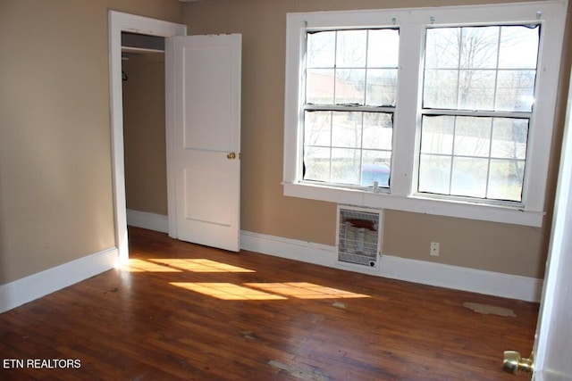 empty room with baseboards, wood finished floors, and heating unit