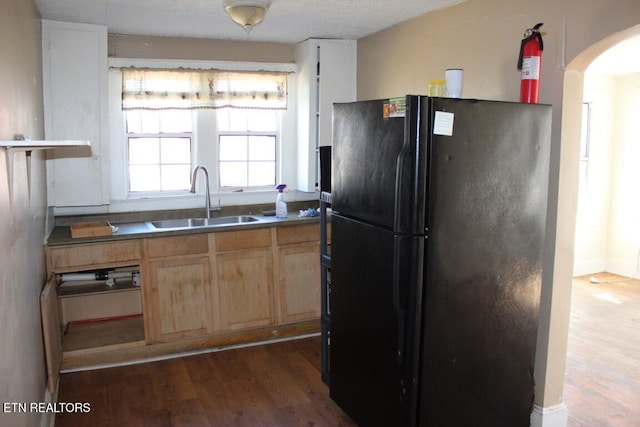 kitchen featuring arched walkways, dark wood finished floors, freestanding refrigerator, light brown cabinetry, and a sink