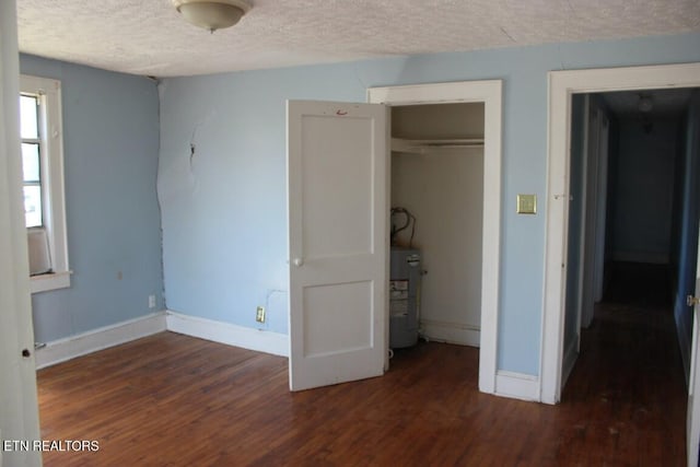 unfurnished bedroom featuring a textured ceiling, electric water heater, dark wood-style flooring, baseboards, and a closet