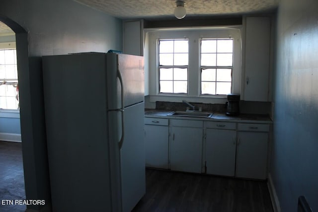 kitchen with arched walkways, dark countertops, freestanding refrigerator, a textured ceiling, and a sink