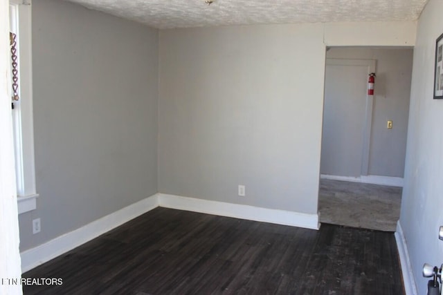 spare room with a textured ceiling, dark wood-style flooring, and baseboards