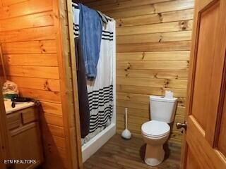 bathroom featuring a stall shower, wooden walls, toilet, and vanity