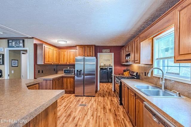 kitchen featuring stainless steel appliances, light countertops, light wood-style floors, brown cabinetry, and a sink