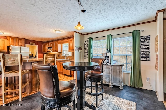 bar with decorative light fixtures, crown molding, freestanding refrigerator, a sink, and a textured ceiling