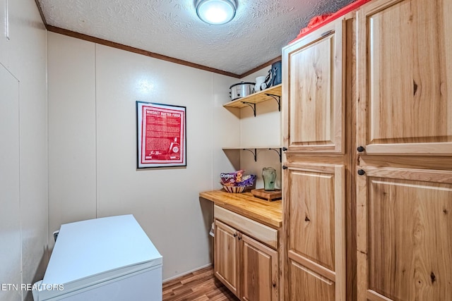 washroom featuring light wood-type flooring, laundry area, ornamental molding, and a textured ceiling