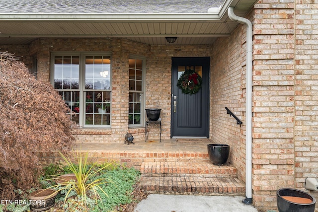 view of exterior entry with brick siding and roof with shingles