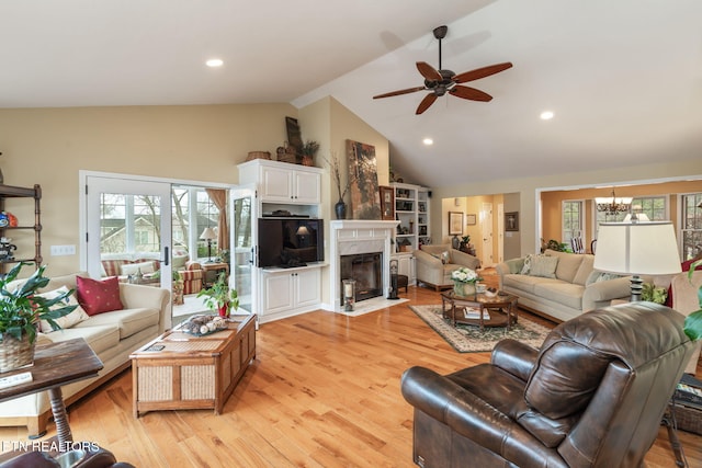 living area with high vaulted ceiling, a premium fireplace, recessed lighting, ceiling fan with notable chandelier, and light wood-type flooring