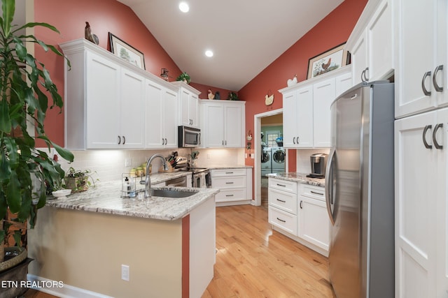 kitchen featuring vaulted ceiling, separate washer and dryer, appliances with stainless steel finishes, white cabinetry, and a sink