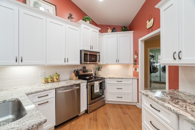 kitchen with washer and clothes dryer, tasteful backsplash, white cabinetry, appliances with stainless steel finishes, and light wood finished floors