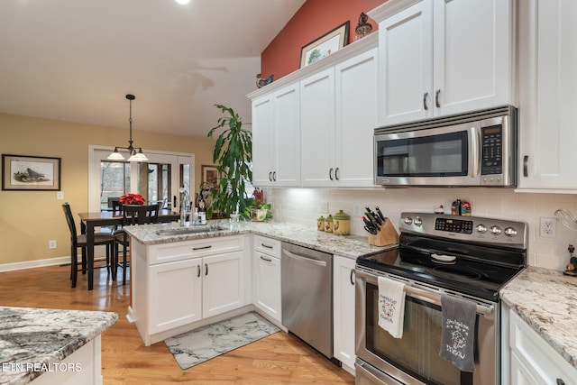 kitchen with a peninsula, a sink, decorative backsplash, appliances with stainless steel finishes, and white cabinetry