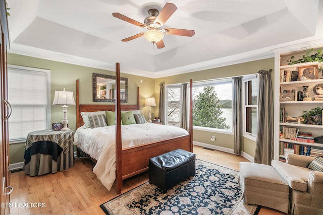 bedroom featuring visible vents, light wood-style flooring, crown molding, and a tray ceiling