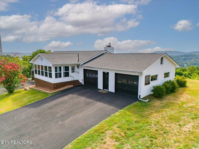 view of front of house featuring an attached garage, a sunroom, driveway, a chimney, and a front yard