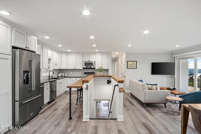 kitchen with decorative backsplash, appliances with stainless steel finishes, open floor plan, white cabinetry, and wooden counters