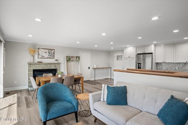 living area featuring visible vents, baseboards, light wood-style flooring, a stone fireplace, and recessed lighting