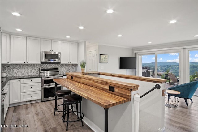 kitchen with stainless steel appliances, butcher block countertops, backsplash, and white cabinetry