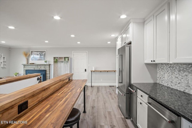 kitchen with appliances with stainless steel finishes, white cabinetry, dark stone counters, and a stone fireplace