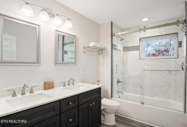 bathroom featuring double vanity, toilet, combined bath / shower with glass door, and a sink