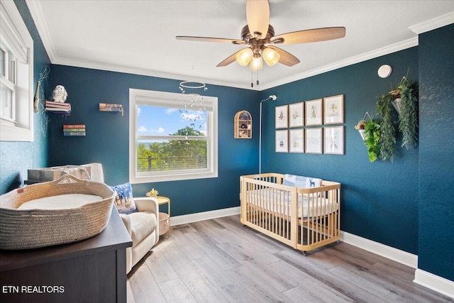 bedroom featuring light wood-style flooring, ornamental molding, a ceiling fan, a crib, and baseboards