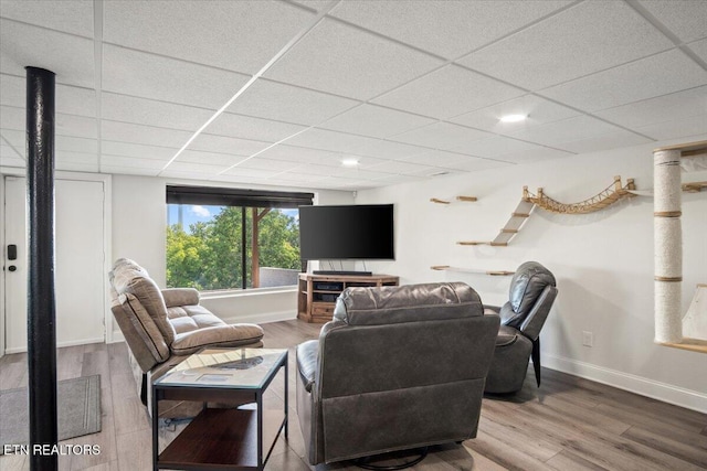 living room featuring a paneled ceiling, baseboards, and wood finished floors