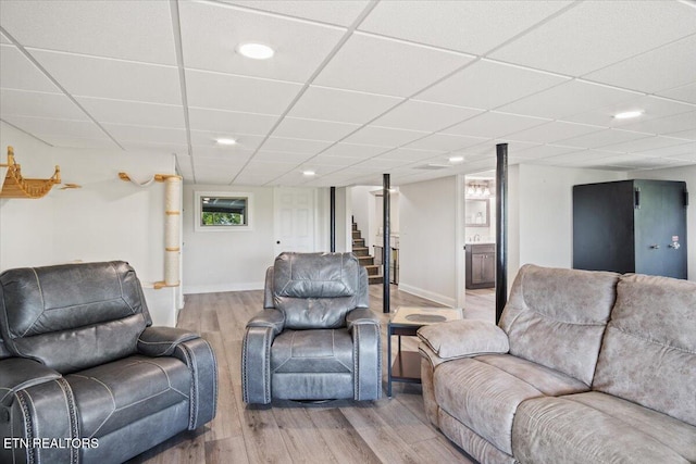 living room featuring stairway, light wood-type flooring, a paneled ceiling, and baseboards