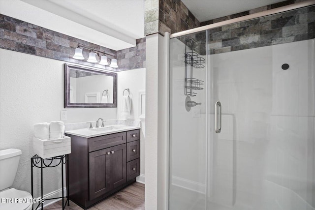 full bathroom featuring a textured wall, toilet, wood finished floors, vanity, and a stall shower