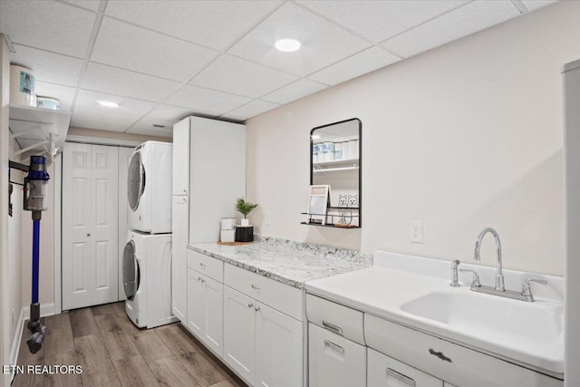 washroom featuring a sink, stacked washer / drying machine, and wood finished floors