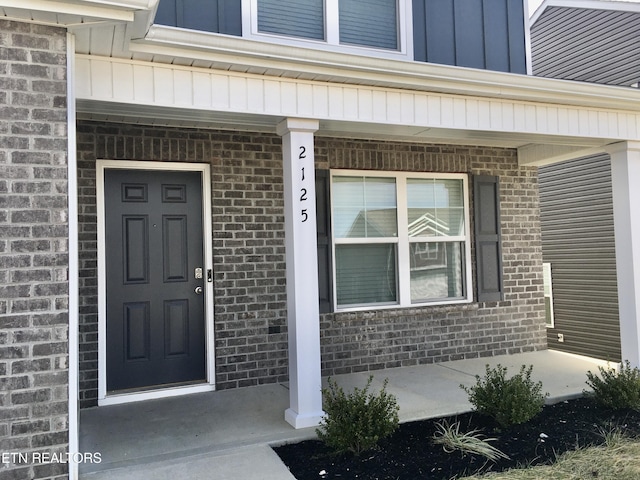 view of exterior entry featuring covered porch, brick siding, and board and batten siding