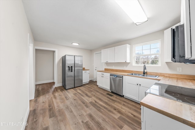 kitchen with stainless steel appliances, light wood-style flooring, white cabinetry, a sink, and butcher block countertops