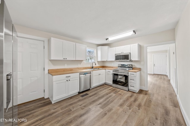 kitchen featuring stainless steel appliances, butcher block countertops, light wood-style flooring, and white cabinetry