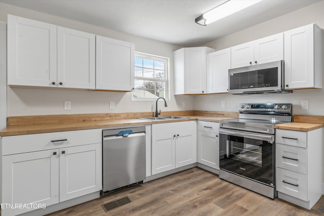 kitchen with a sink, white cabinets, light wood-style floors, wooden counters, and appliances with stainless steel finishes