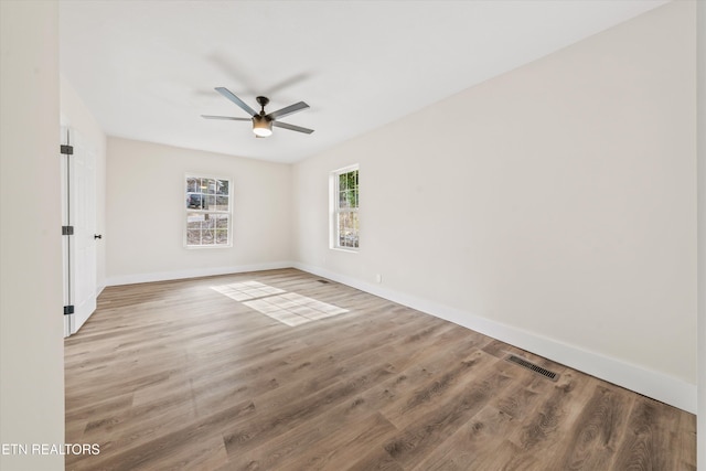 empty room with a ceiling fan, wood finished floors, visible vents, and baseboards