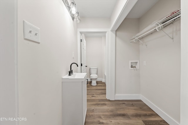 bathroom with a walk in closet, toilet, vanity, wood finished floors, and baseboards