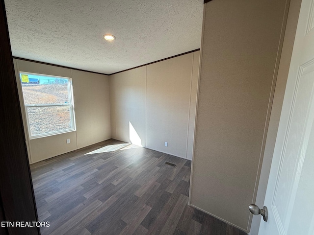 spare room featuring dark wood-style floors, a textured ceiling, visible vents, and crown molding