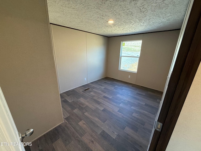 unfurnished room featuring dark wood-style flooring, visible vents, and a textured ceiling