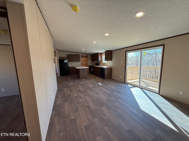 kitchen featuring a kitchen island, open floor plan, dark wood-style flooring, freestanding refrigerator, and light countertops