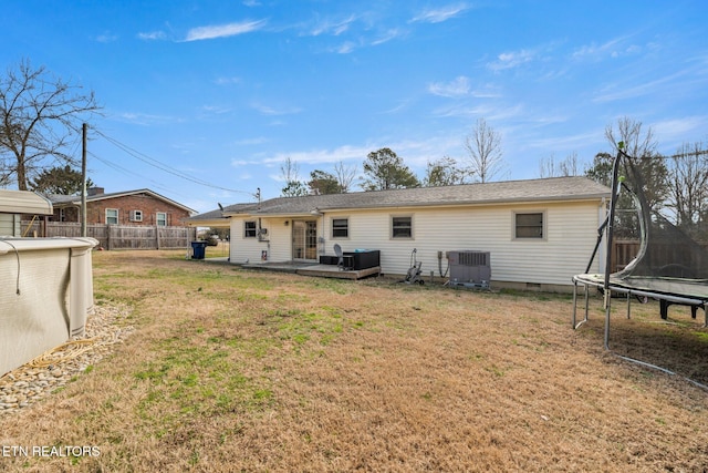 back of house featuring central AC unit, fence, crawl space, a lawn, and a trampoline