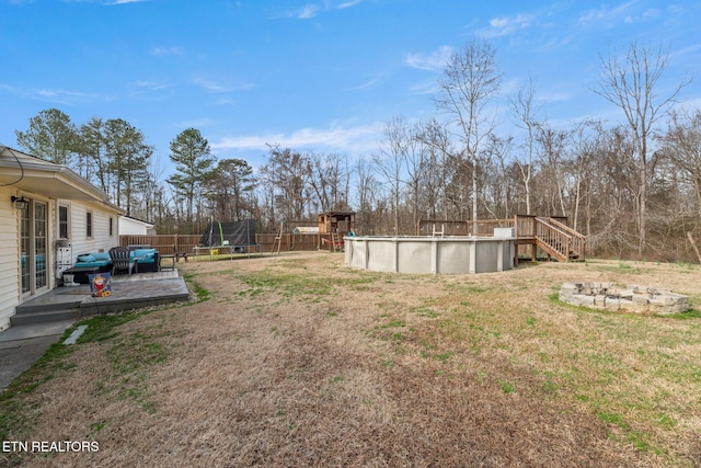 view of yard featuring a fire pit, a fenced in pool, stairs, a trampoline, and fence