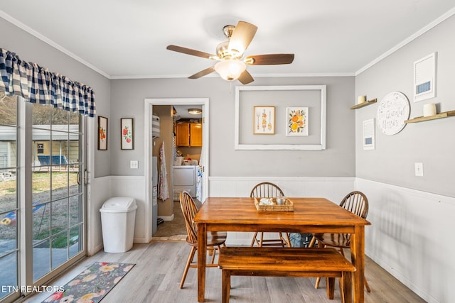 dining space with a wainscoted wall, light wood-style flooring, ceiling fan, ornamental molding, and separate washer and dryer