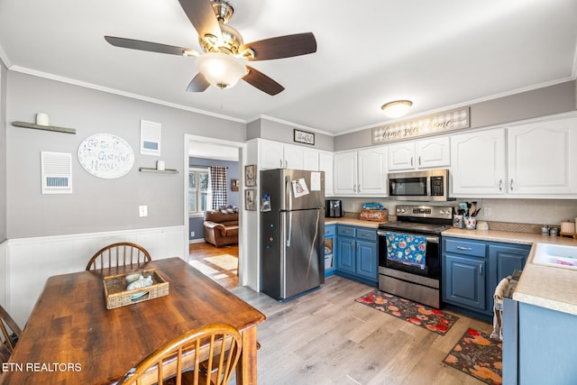 kitchen with blue cabinetry, light countertops, appliances with stainless steel finishes, white cabinets, and wainscoting