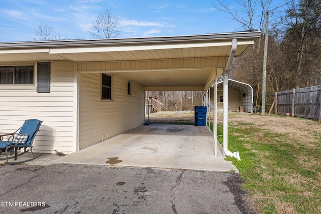 view of vehicle parking with driveway, an attached carport, and fence