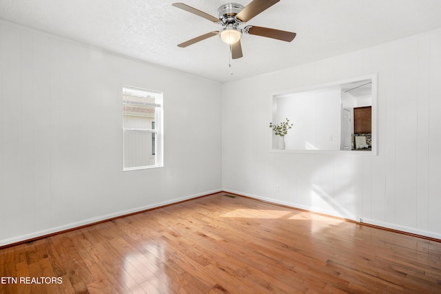 empty room with a textured ceiling, hardwood / wood-style floors, a ceiling fan, and baseboards