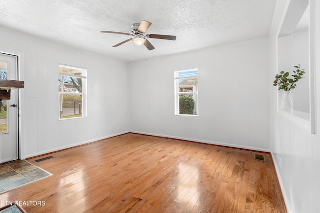 unfurnished room with a textured ceiling, a wealth of natural light, hardwood / wood-style flooring, and visible vents