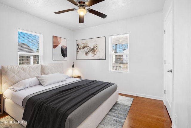 bedroom featuring baseboards, multiple windows, a ceiling fan, and wood finished floors