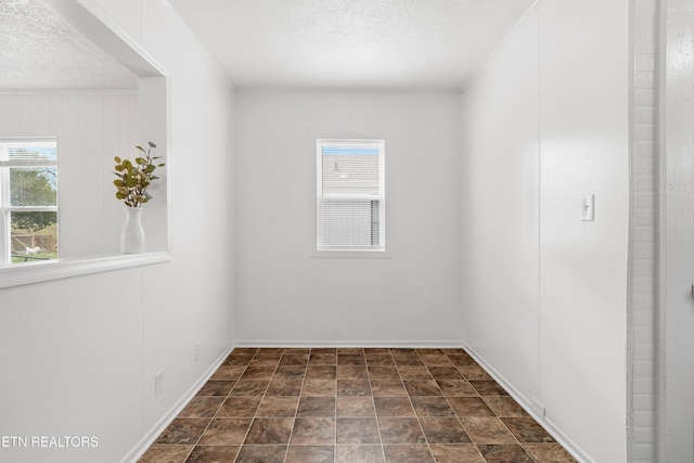 empty room featuring baseboards, ornamental molding, and a textured ceiling