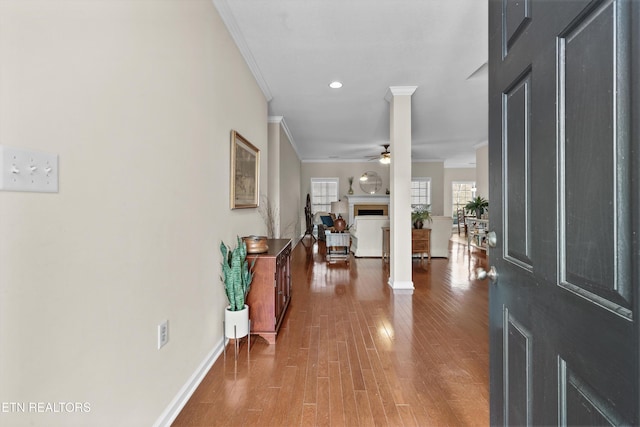 foyer featuring ceiling fan, a fireplace, wood finished floors, baseboards, and crown molding