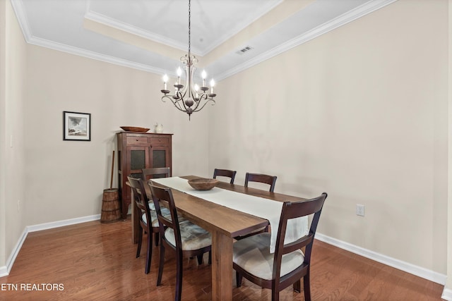 dining space featuring baseboards, visible vents, a tray ceiling, and wood finished floors