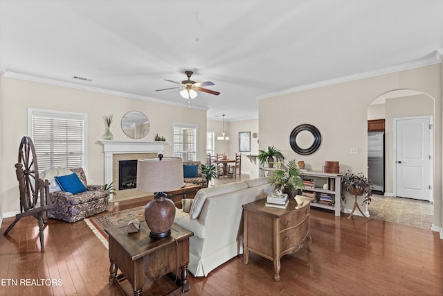 living room featuring baseboards, arched walkways, hardwood / wood-style flooring, a fireplace with flush hearth, and ornamental molding