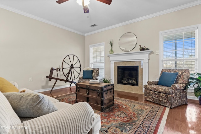 living area featuring a fireplace, visible vents, baseboards, ornamental molding, and wood-type flooring